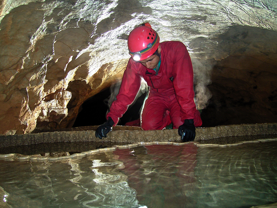 Petite retenue d'eau (gours) dans grotte avec spéléologue.